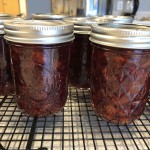 two jelly jars of a dark red jam on a wire cooling rack
