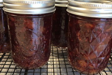 two jelly jars of a dark red jam on a wire cooling rack
