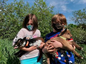2 children holding 2 baby goats