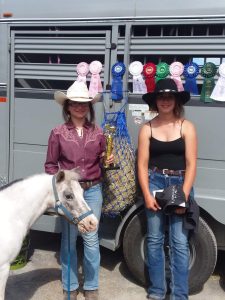 Two 4-H youth with a mini horse and a collection of fair ribbons