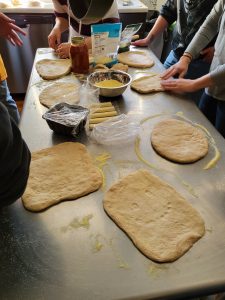 Eight pizza doughs being shaped by adult participants