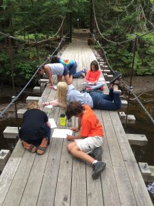 4-H youth campers drawing pictures while relaxing on a bridge at camp