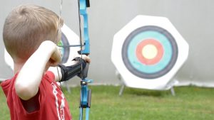 camper takes aim at target with bow and arrow