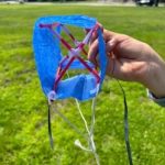 person holding a handmade kite, blue tissue paper with red straws