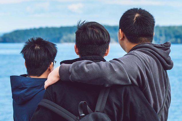 three teenagers with their arms around one another looking out to the ocean