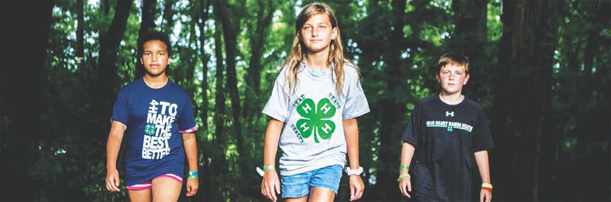 header image for 4-H section of annual report, three teenagers wearing 4-H branded t-shirts taking a walk in the forest