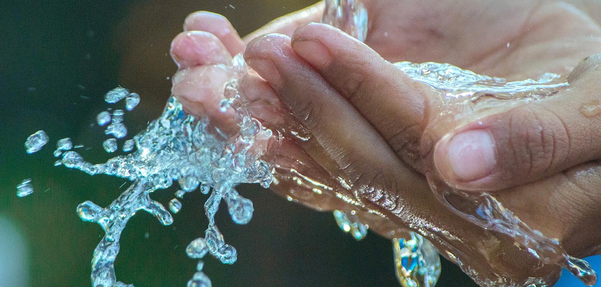 water coming out of a tap and splashing over a outstretched hand - drinking water - banner image for PFAS page