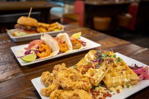 three different plates of pub fare food items: burgers, tacos and chicken with waffles