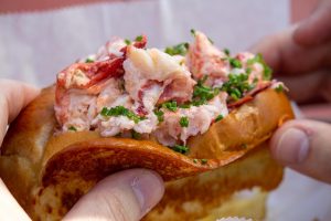 close up of two hands hold each end of a lobster roll