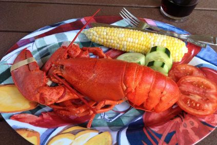 Steamed lobster on a platter with an ear of corn, cucumber and tomato slices