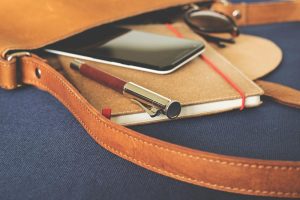 leather messenger bag that contains a notebook, pen and mobile device at a conference