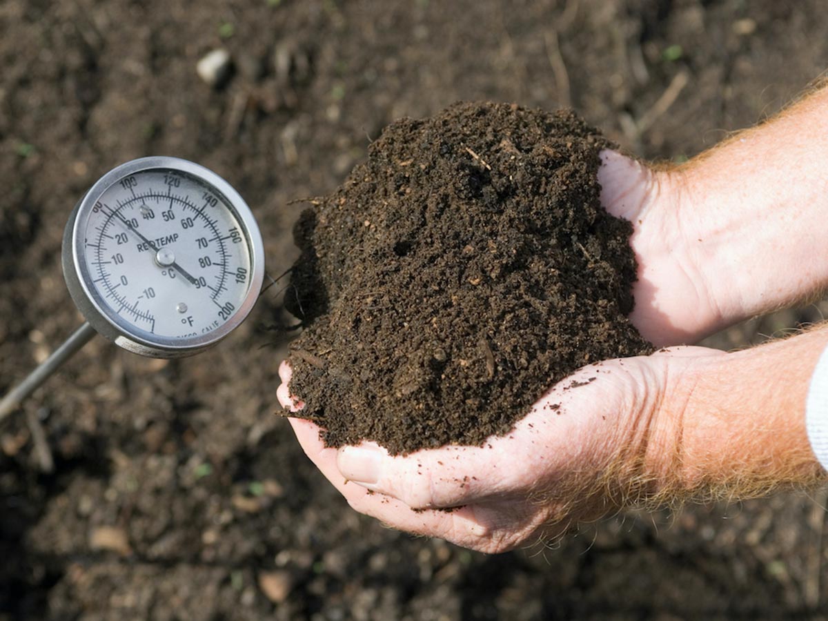 person composting while using a soil thermometer