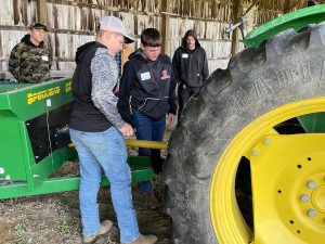 participants at a farm visit learning to attach a tractor implement