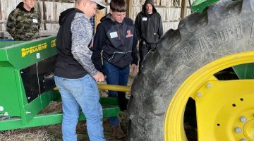 participants at a farm visit learning to attach a tractor implement