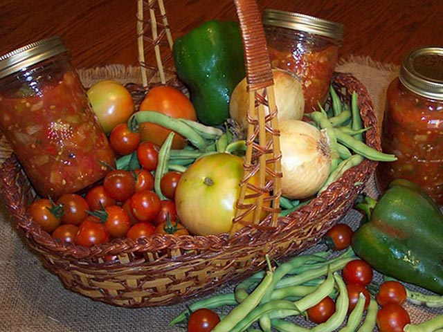 a basket of vegetables from a harvest from the garden along with jars of preserved sauce made from the vegetables