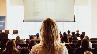 a person facing a presentation at a conference in a crowd of seated participants