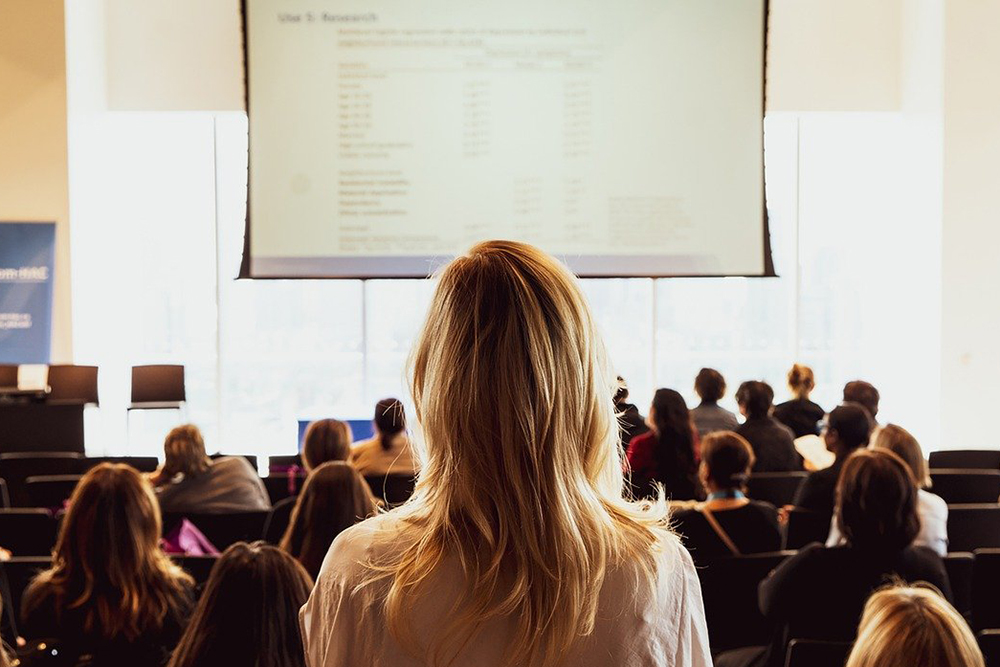 a person facing a presentation at a conference in a crowd of seated participants