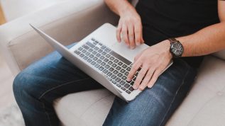 person sitting in a chair with a laptop, typing on a keyboard to submit a form