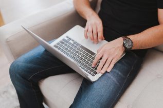 person sitting in a chair with a laptop, typing on a keyboard to submit a form