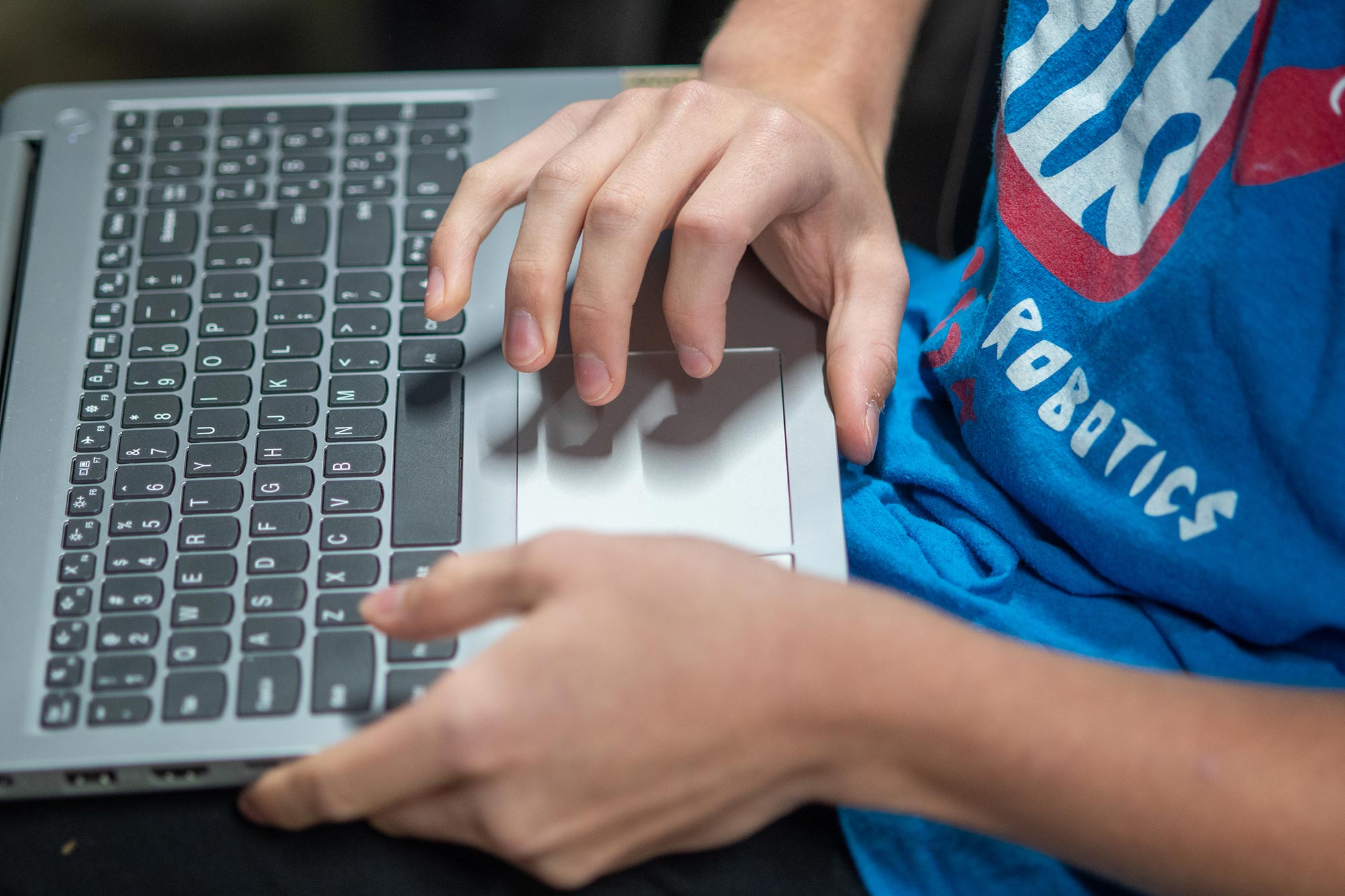 a teenager using a laptop, typing on a keyboard