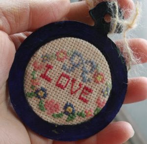 Image of cross stitch of the word love with a blue ribbon and flowers