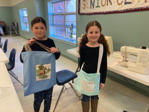 Two girls hold homemade tote bags
